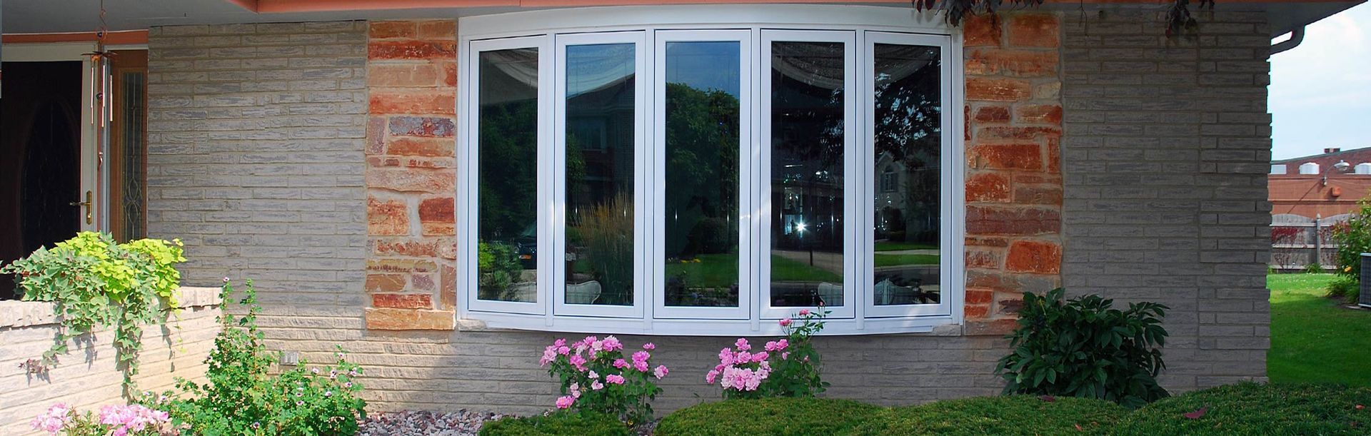 A window in a brick and stucco house, with green grass and pink flowers in front.
