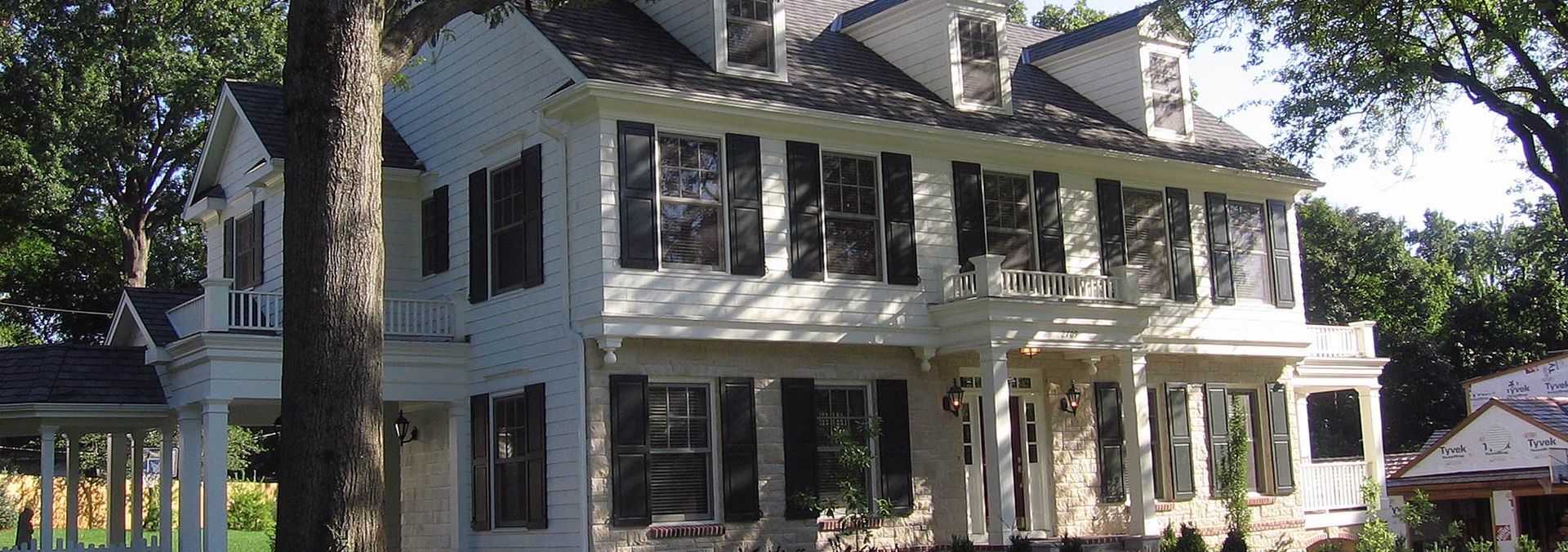White Victorian house with black shutters, surrounded by trees.