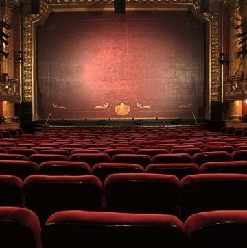 an empty auditorium with red seats and a stage in the background .
