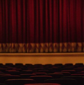 a row of empty seats in an auditorium with a red curtain behind them .