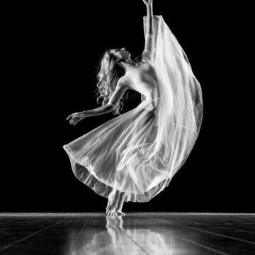 a black and white photo of a ballerina in a white dress dancing on a stage .