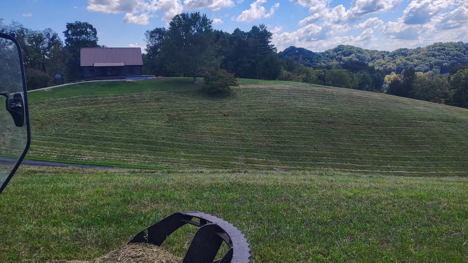 A grassy, sloped field leads to a small barn near a tree line under a blue sky with scattered clouds.
