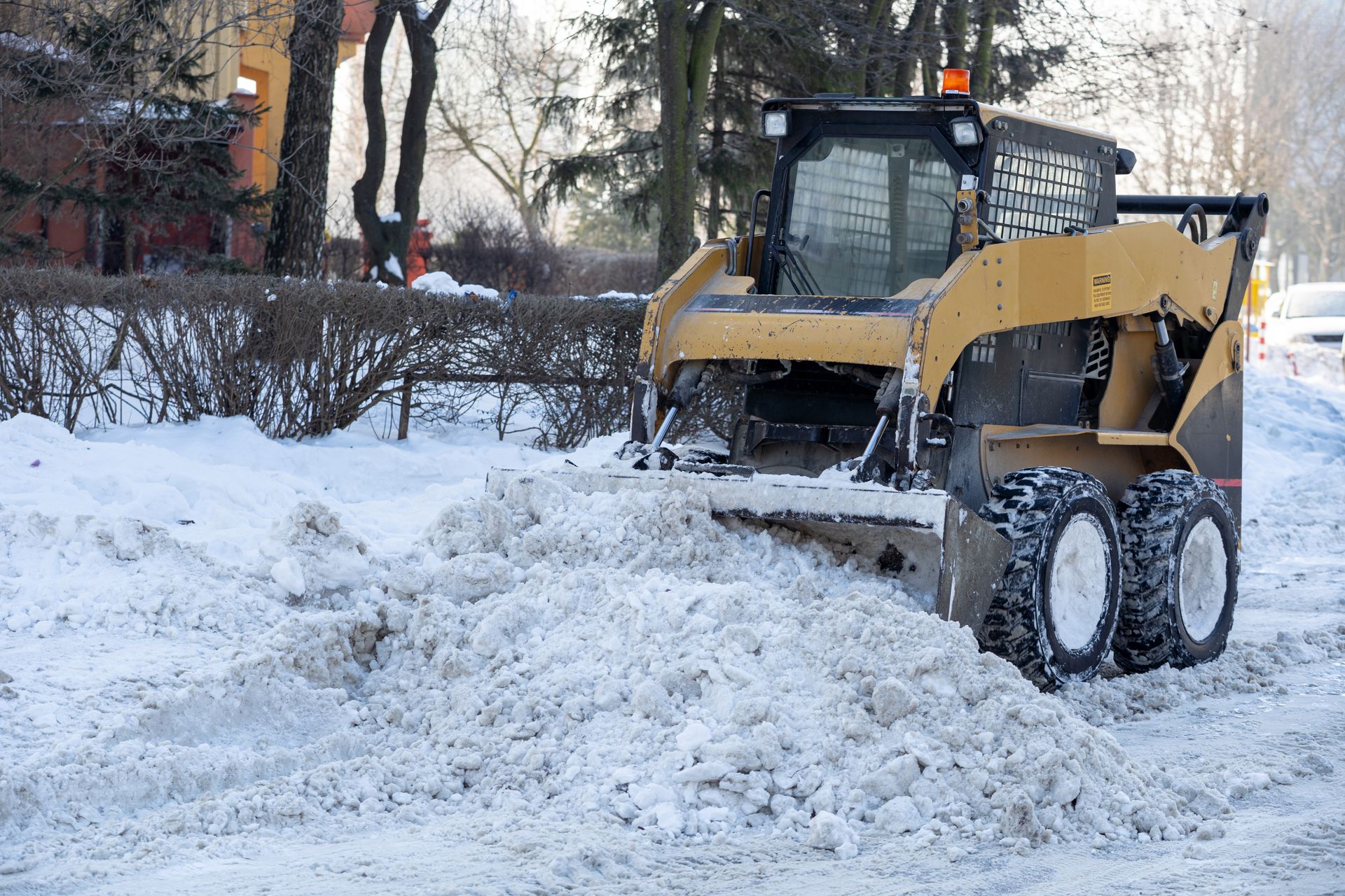 A yellow skid steer loader clearing snow from a street during the day.