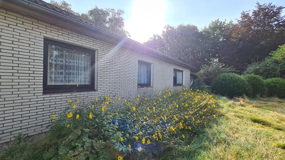 Ein weißes Backsteinhaus mit vielen Blumen davor.