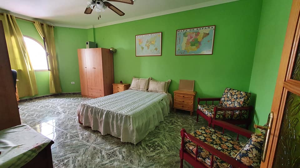 Ein Schlafzimmer mit grünen Wänden, einem Bett, einem Stuhl und einem Deckenventilator.