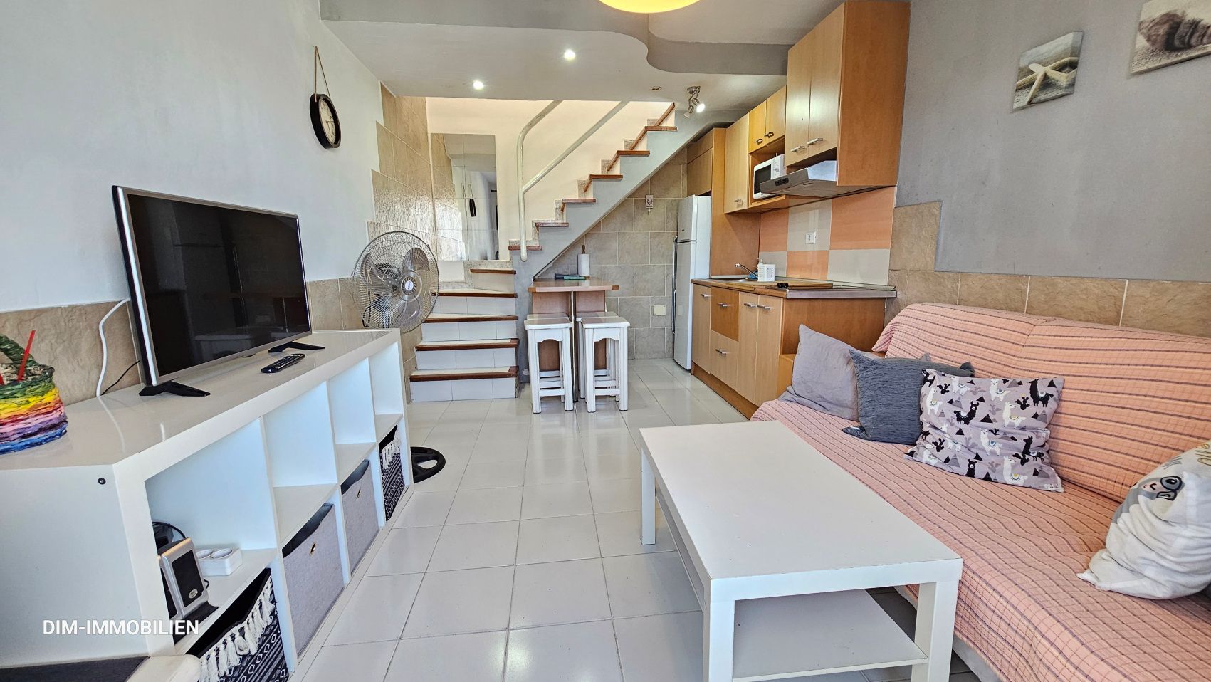 Ein Wohnzimmer mit Couch, Tisch, Fernseher und Treppe.