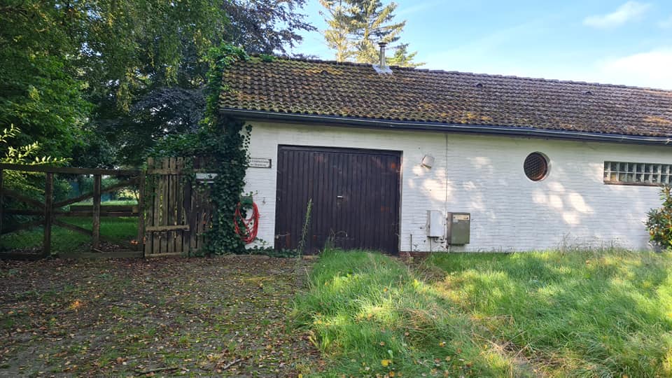 Eine weiße Garage mit einem braunen Tor steht inmitten einer Wiese.