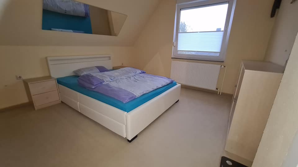 Ein Schlafzimmer mit Bett, Nachttisch, Spiegel und Fenster.