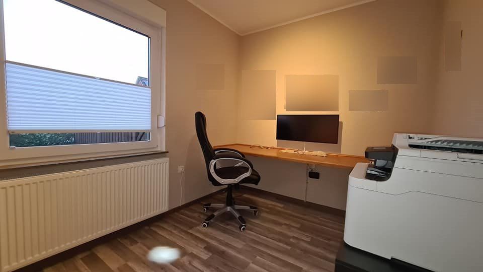 Ein Raum mit Schreibtisch, Stuhl, Computer und Drucker.