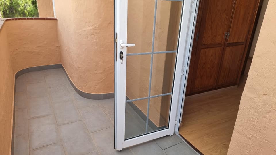 Eine weiße Tür führt auf einen Balkon, hinter dem sich eine Holztür befindet.