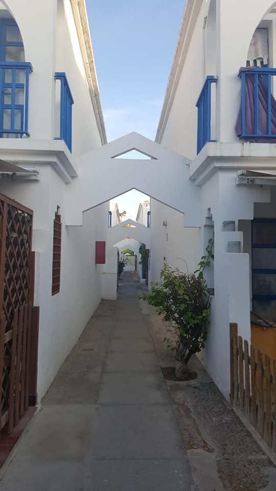 Eine schmale Gasse zwischen zwei weißen Gebäuden mit blauen Balkonen.