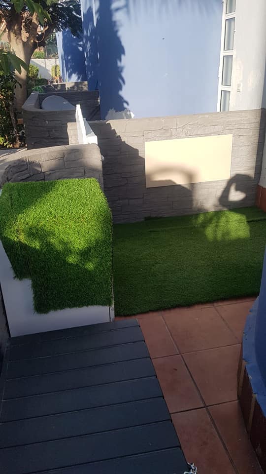 Eine Terrasse mit Backsteinmauer und Rasen vor einem Haus.