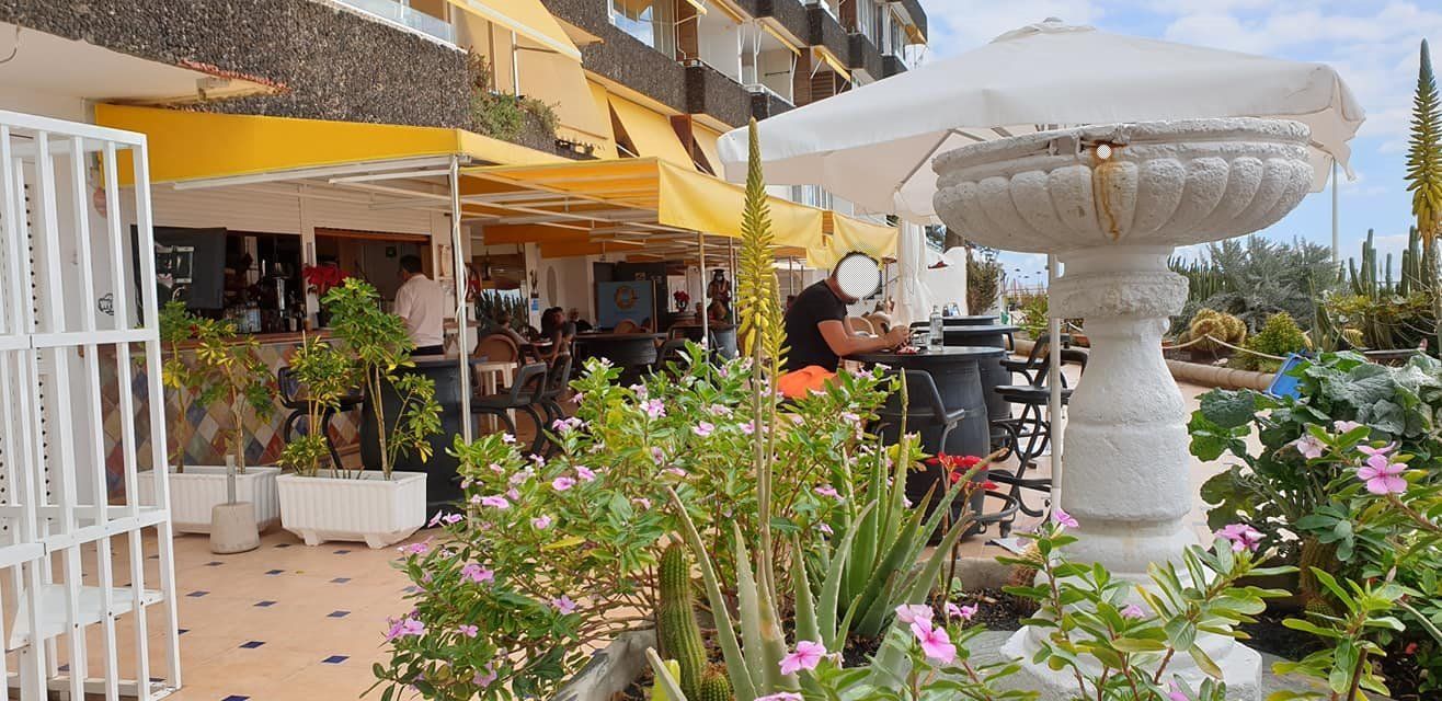 Ein Brunnen vor einem Restaurant mit Leuten, die unter Sonnenschirmen an Tischen sitzen.