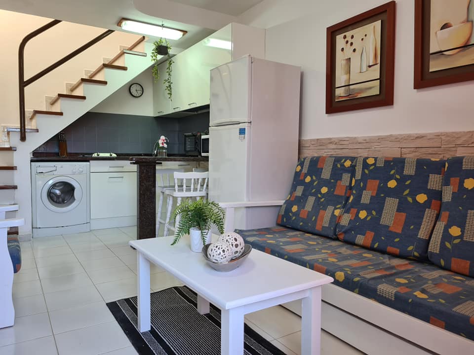 Ein Wohnzimmer mit Couch, Tisch, Kühlschrank und Treppe zur Küche.