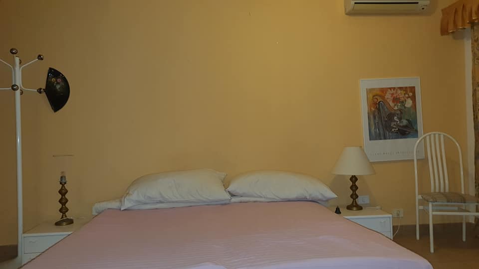 Ein Schlafzimmer mit Bett, Stuhl, Nachttisch, Lampe und Klimaanlage.