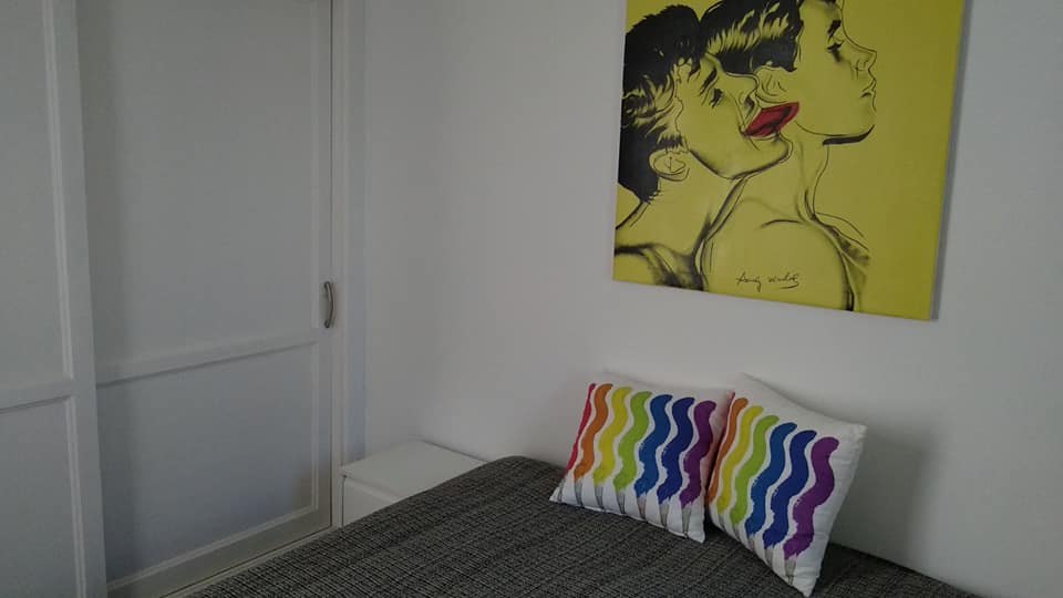 An der Wand über dem Bett hängt ein Gemälde von zwei sich küssenden Frauen.