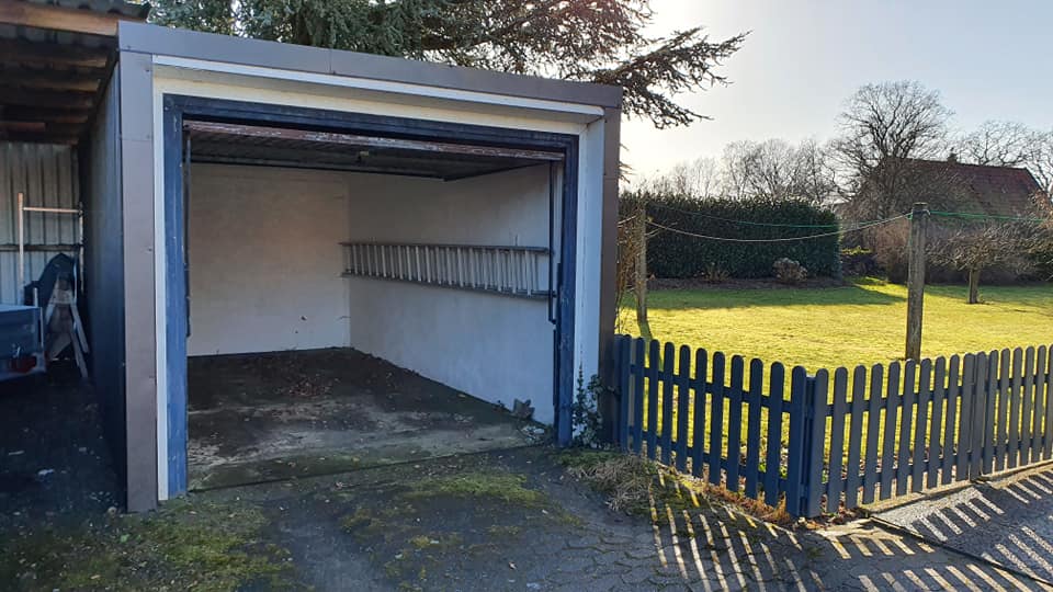 Eine Garage mit einer Leiter darin und einem Zaun darum herum.