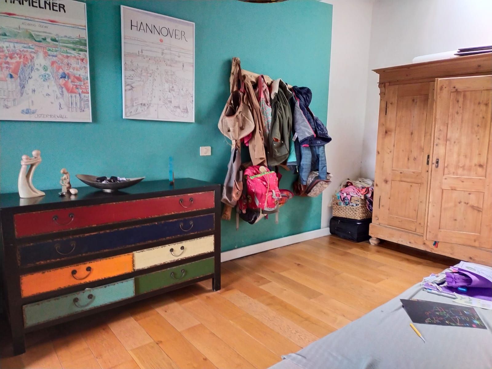 Ein Zimmer mit einer Kommode und einem Kleiderschrank mit an der Wand hängender Kleidung.