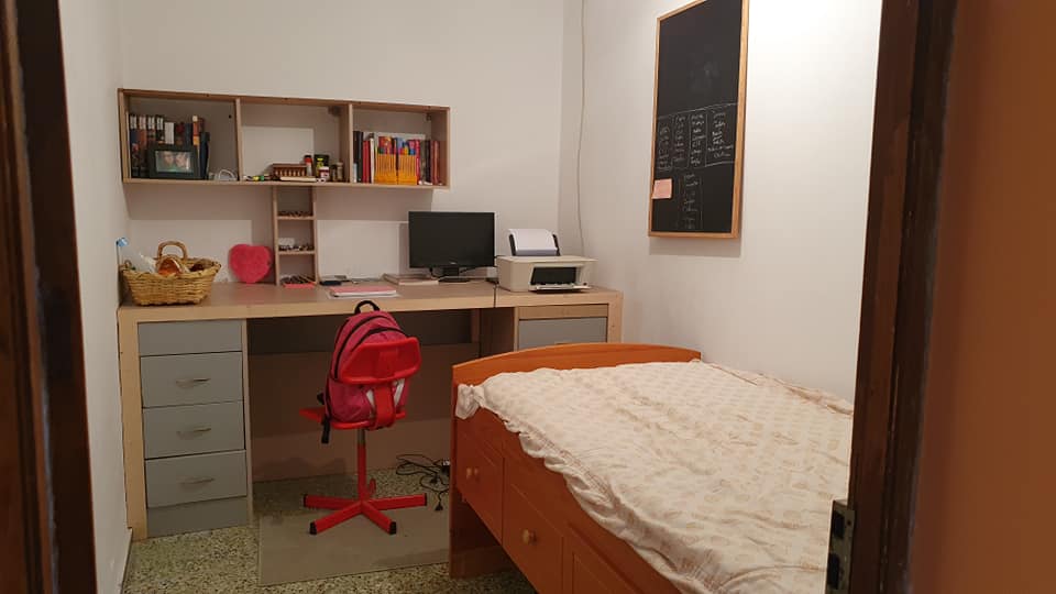 Ein Schlafzimmer mit Bett, Schreibtisch, Computer und Drucker.