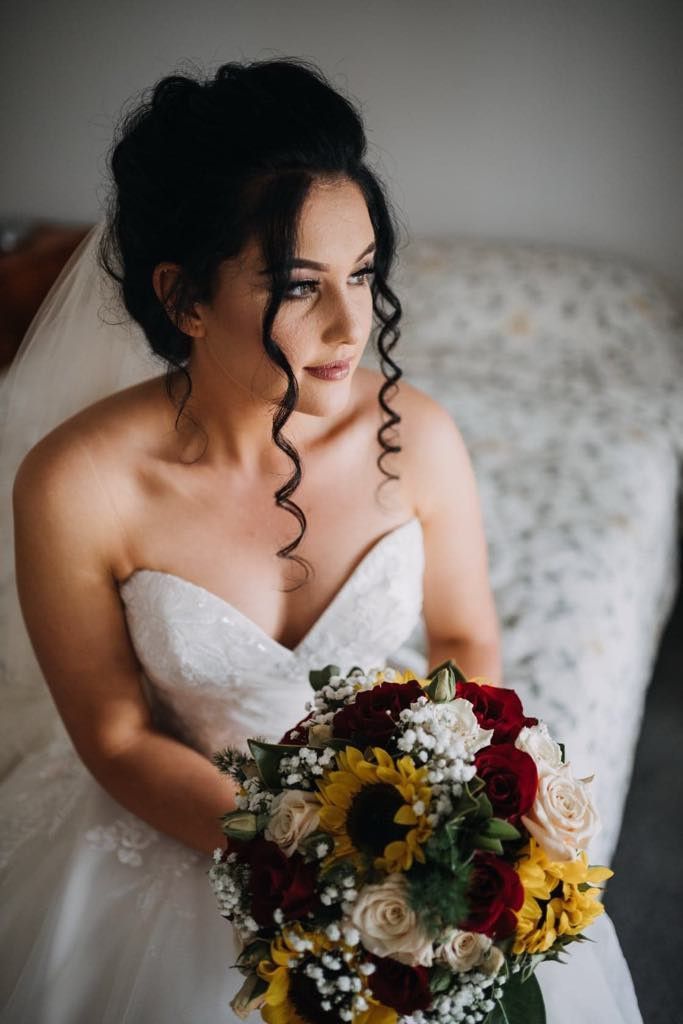A Bride in a Wedding Dress is Sitting on a Bed Holding a Bouquet of Flowers — Xquisite Styles in Mount Warrigal, NSW
