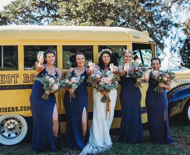 A Bride and Her Bridesmaids Are Posing for a Picture in Front of a Yellow Bus — Xquisite Styles in Mount Warrigal, NSW