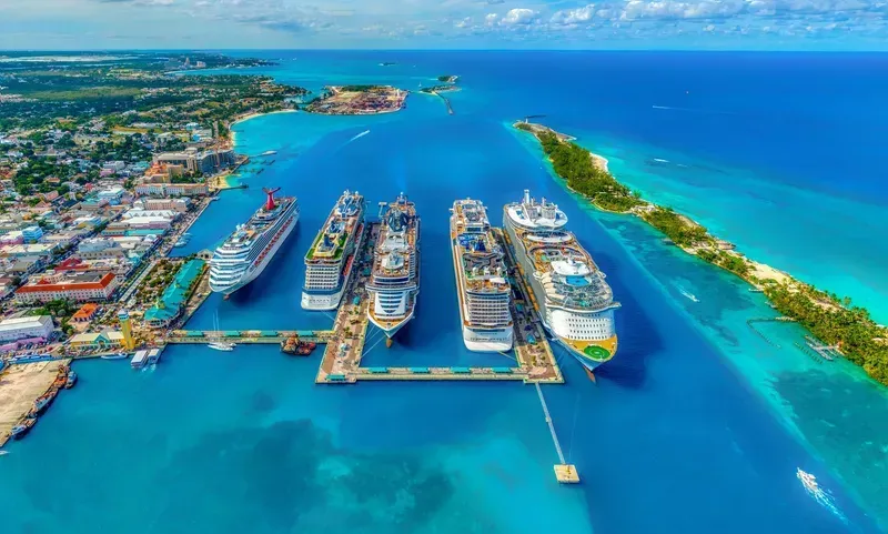 Aerial view of a cruise ship port with several large ships docked in bright turquoise water near a tropical coastline