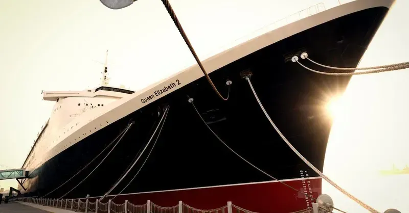 Large white and black ship docked at sunset, with sun glare on the bow.
