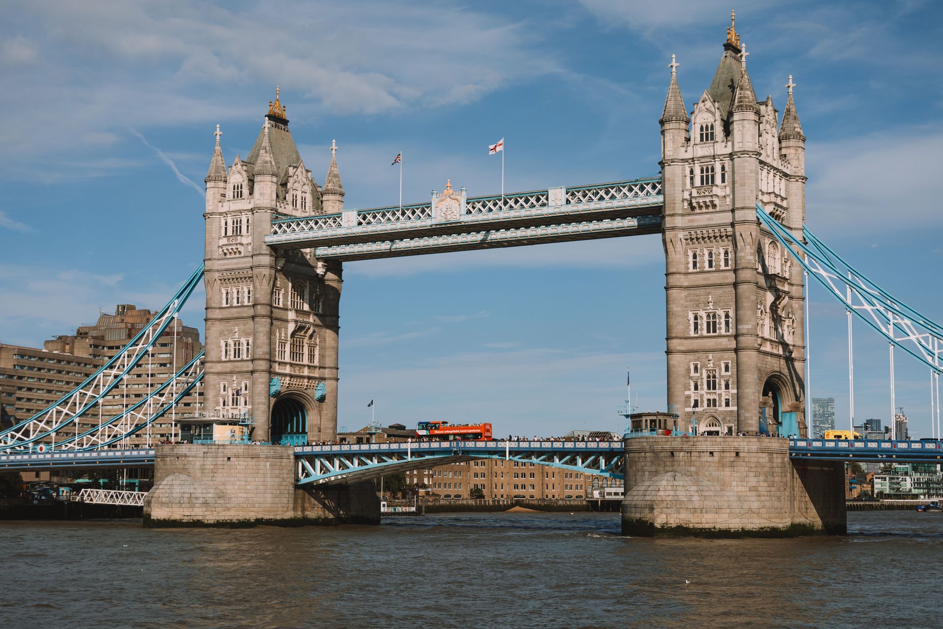 Tower Bridge over the River Thames in London, with a red double-decker bus crossing and a clear blue sky.