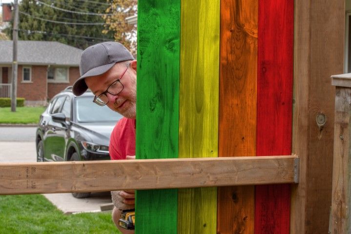 Man painting a rainbow-colored fence in a residential setting.