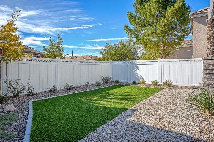 Backyard with white fence, artificial turf lawn, gravel, and blue sky.