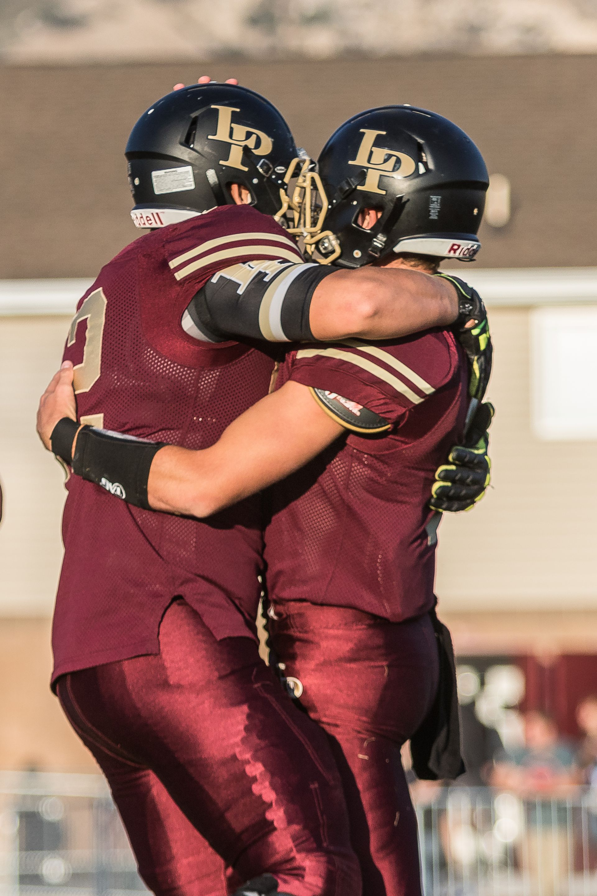 Football player in maroon jersey holding ball, smiling, surrounded by teammates on a field.