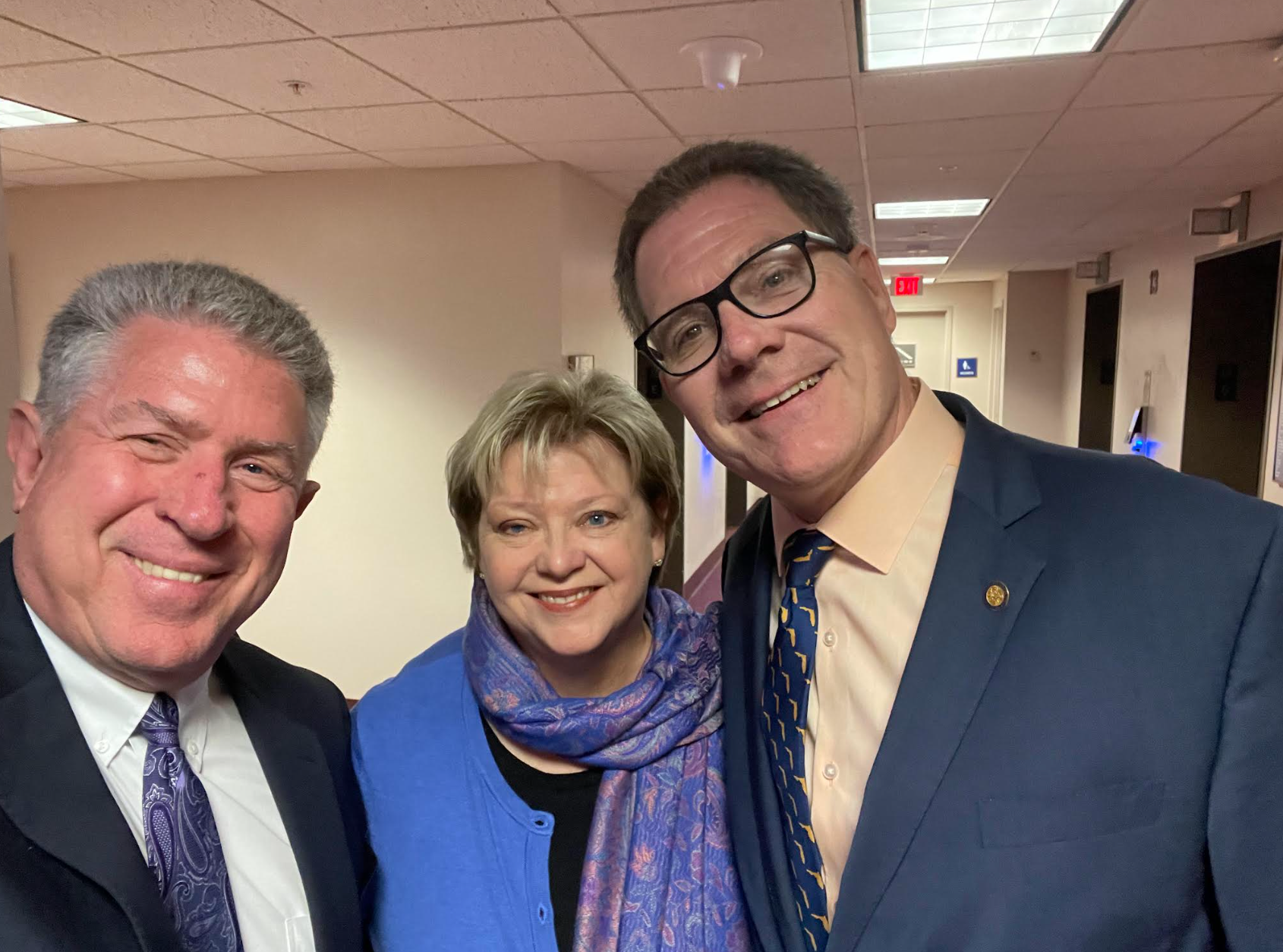 Two men and a woman are posing for a picture in a hallway.