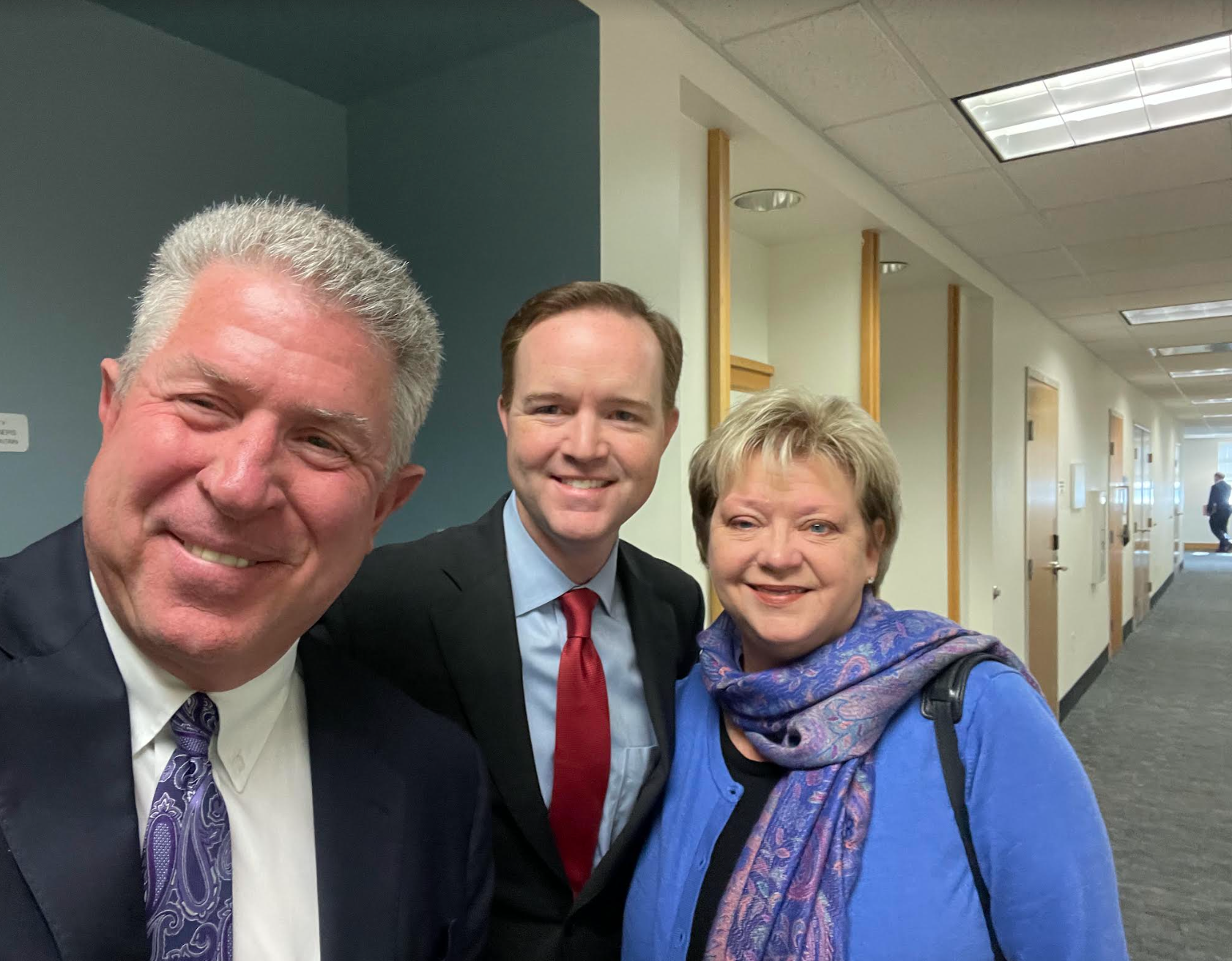 Three people are posing for a picture in a hallway.