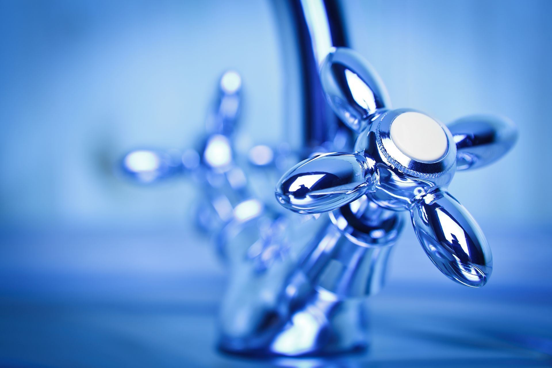 A chrome faucet handle with a star-shaped design, set against a soft, blue-toned background.