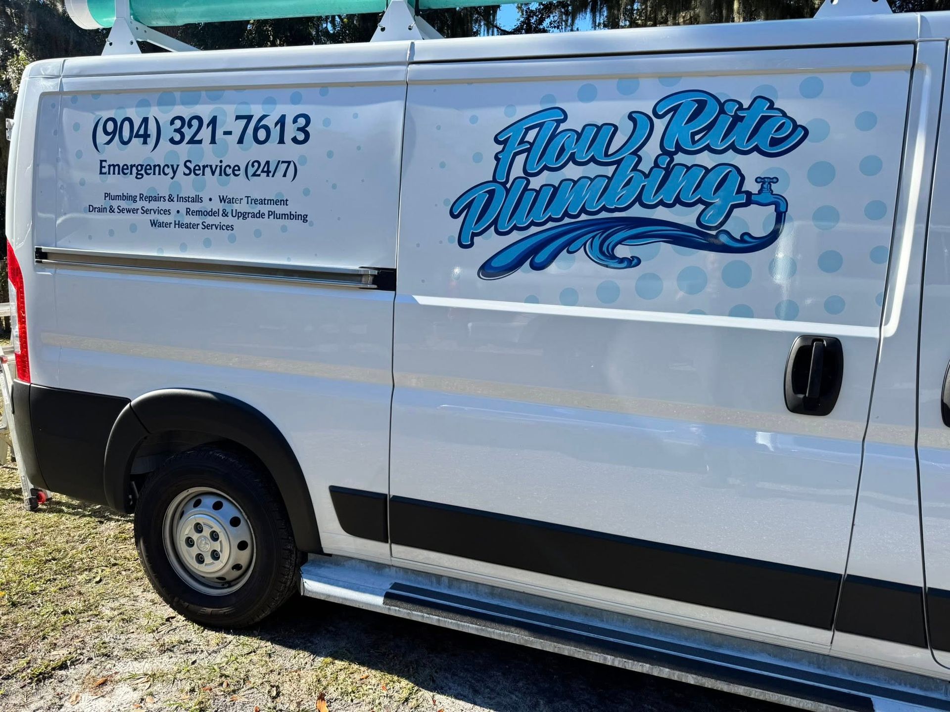 A white Flow Rite Plumbing work van featuring a blue logo and company phone number, parked on grass.