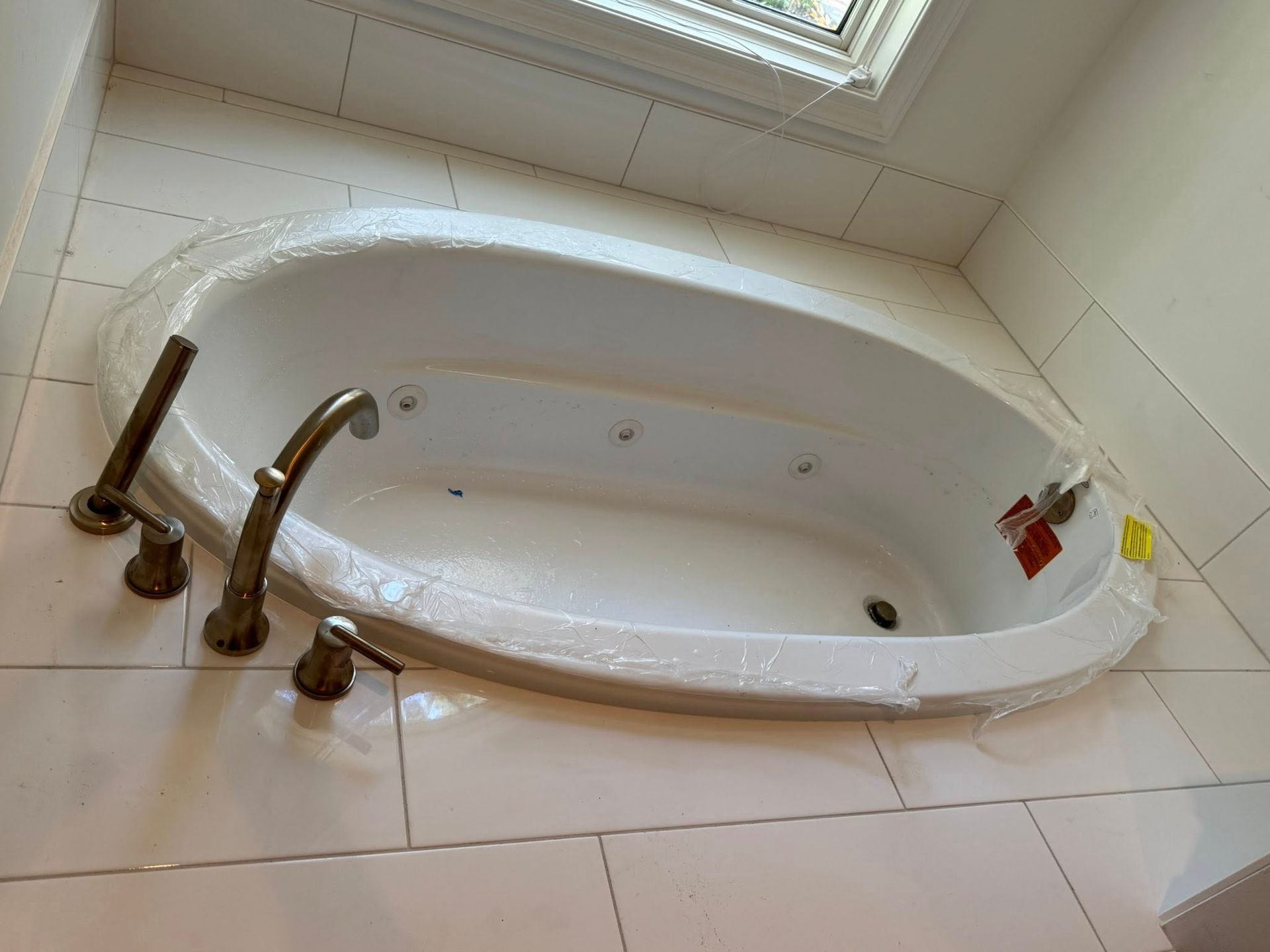 An oval, jetted white bathtub with bronze fixtures installed in a tiled bathroom deck.
