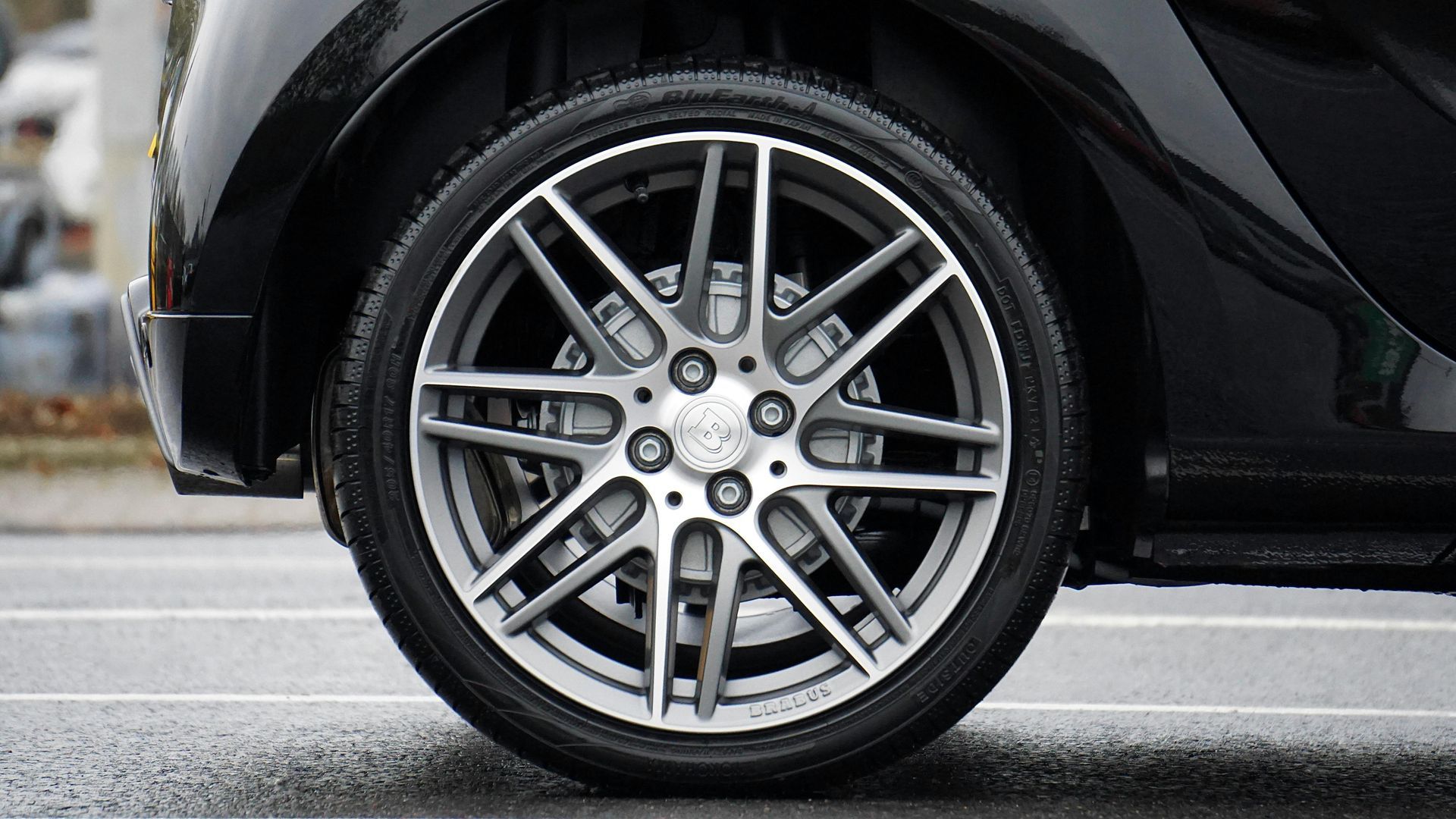 Black car's silver alloy wheel on a wet street.