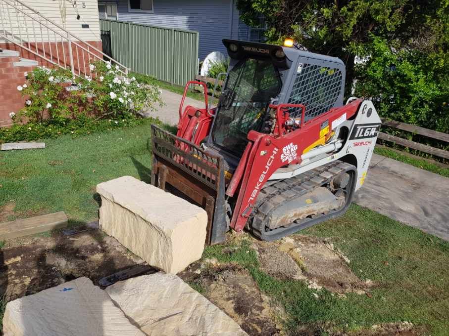 Small Red Excavator Lifting Cement Block — Stan Davies Excavations in Glendale, NSW