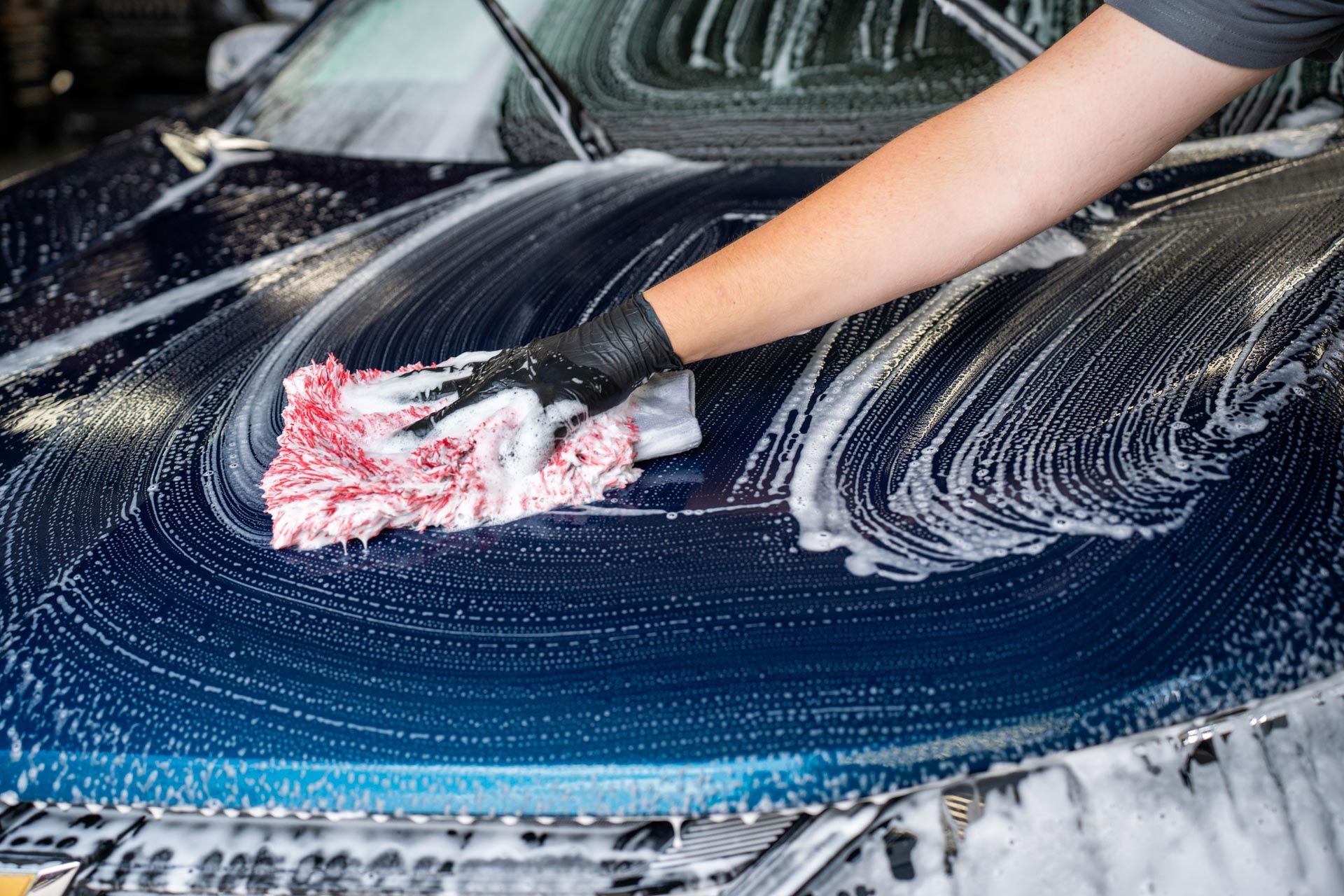 Person washing a dark blue car with a soapy cloth.