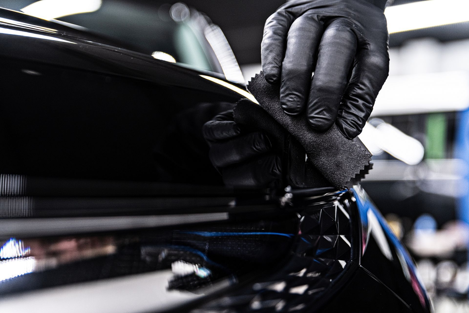 Gloved hand applying a ceramic coating to a black car surface with a microfiber applicator.