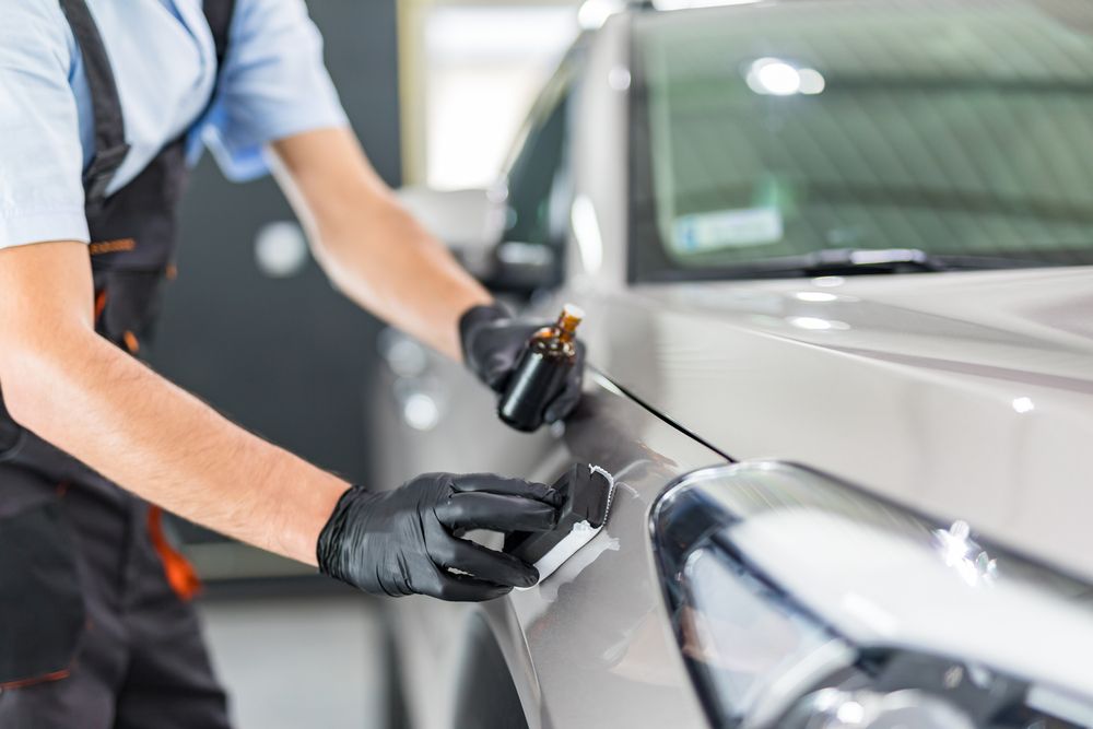 A person in black gloves applies ceramic coating to a silver car's fender.