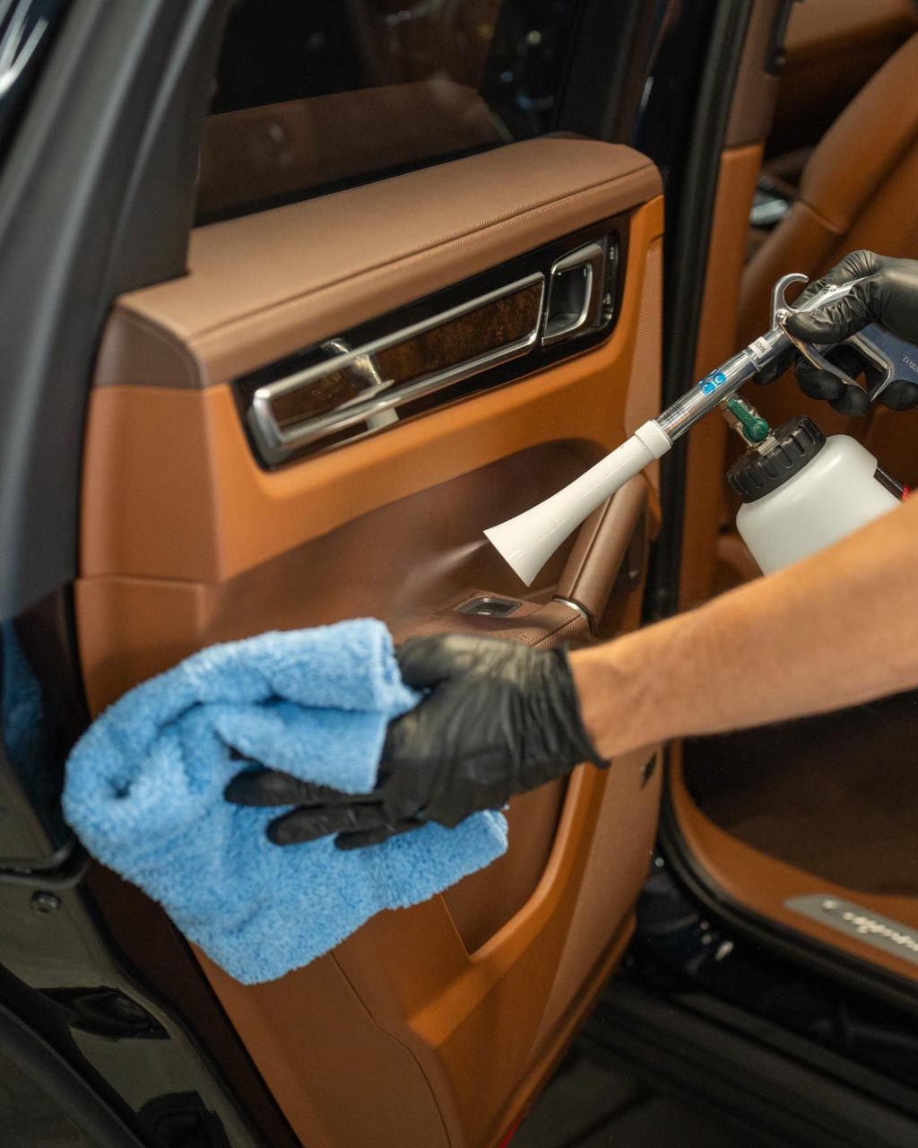 Person cleaning car door panel with a spray gun and blue cloth.