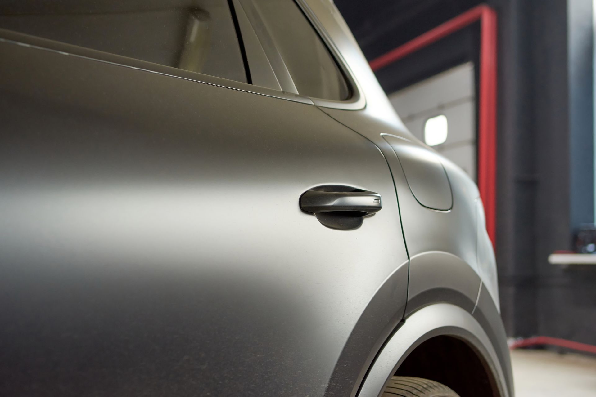 Matte gray car door with black handle and wheel arch in a garage setting.