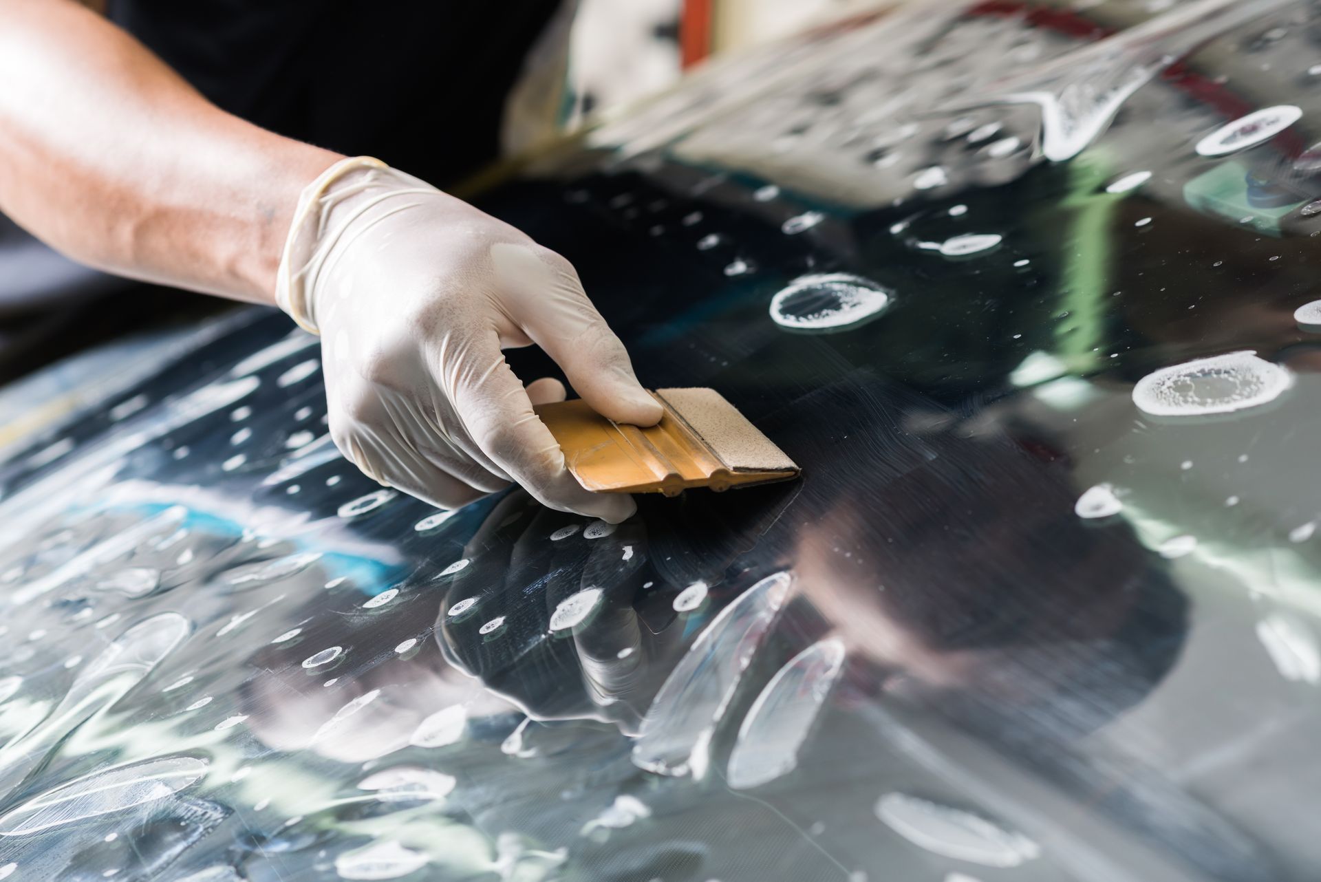 Gloved hand uses a squeegee to apply tinted film to a surface, removing bubbles.