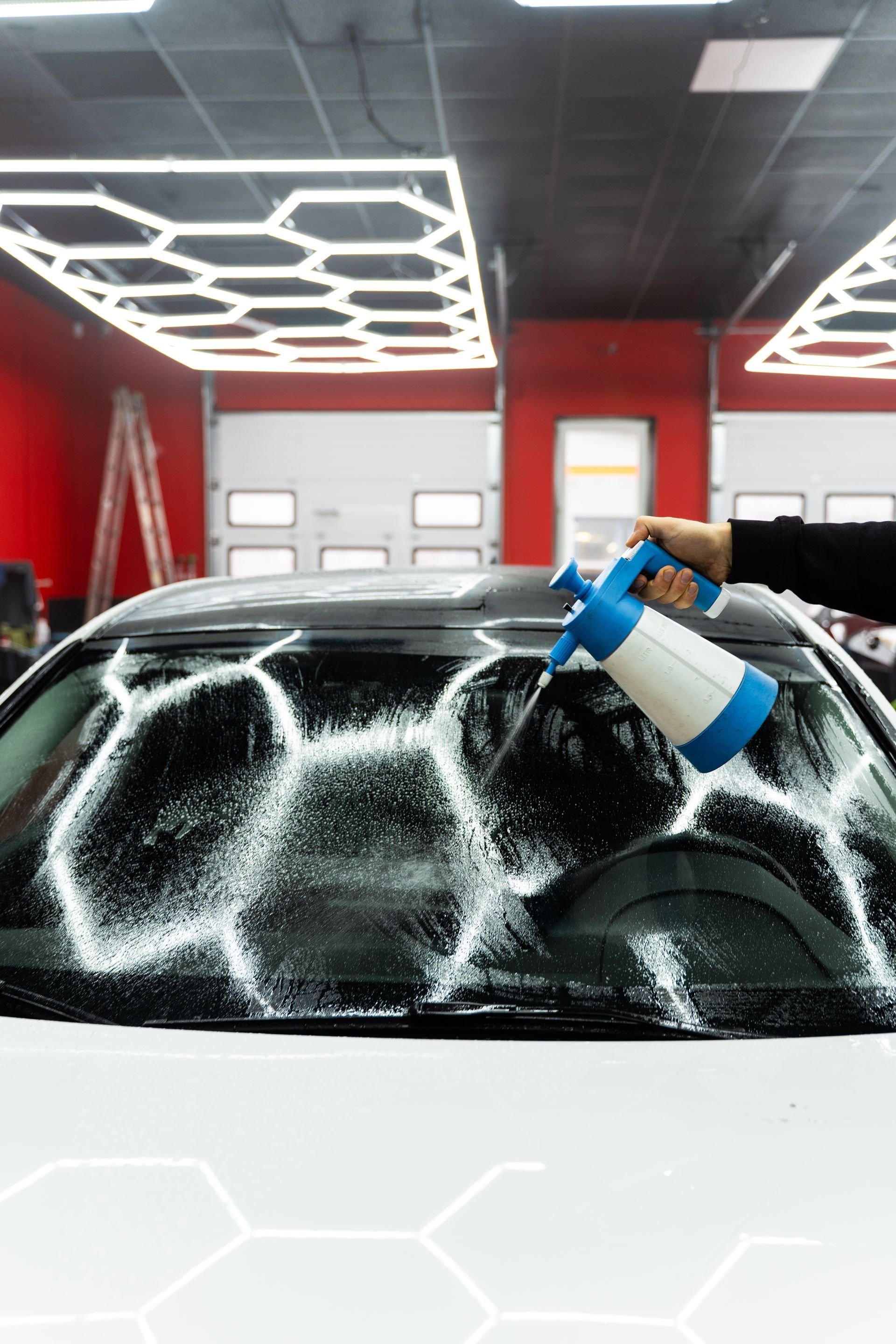 Person spraying soapy water on a car windshield in a garage.