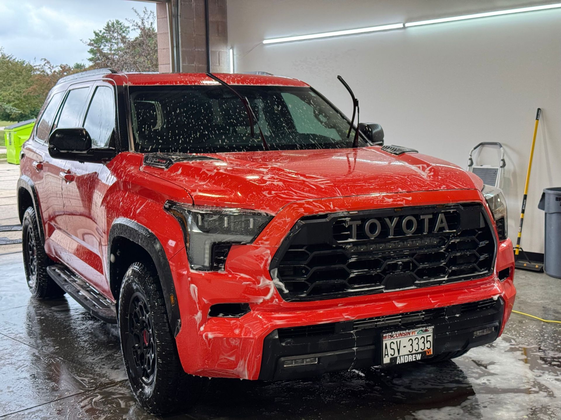Red Toyota Sequoia SUV covered in soap suds at a car wash.