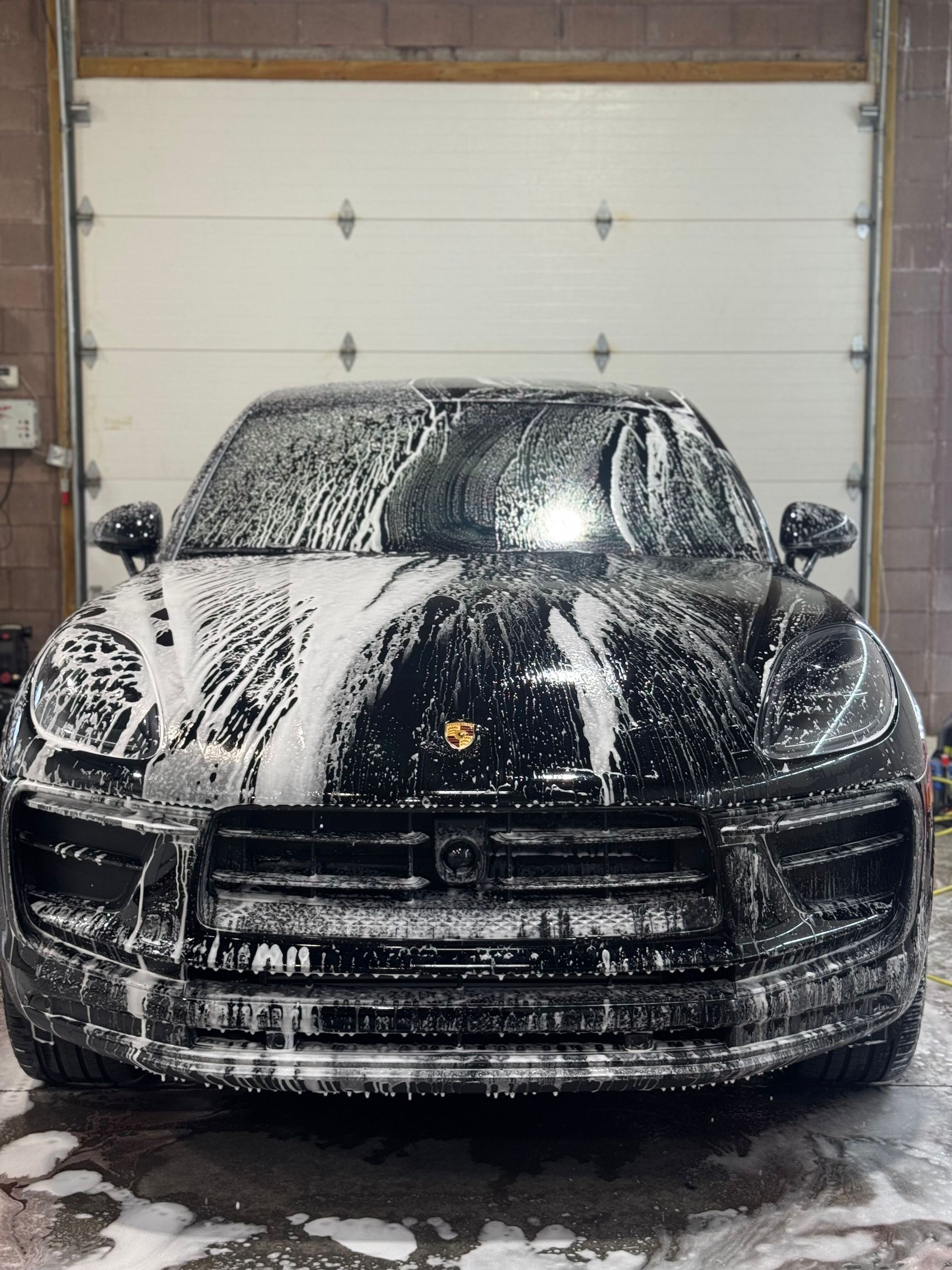 Black Porsche SUV covered in white foam at a car wash.
