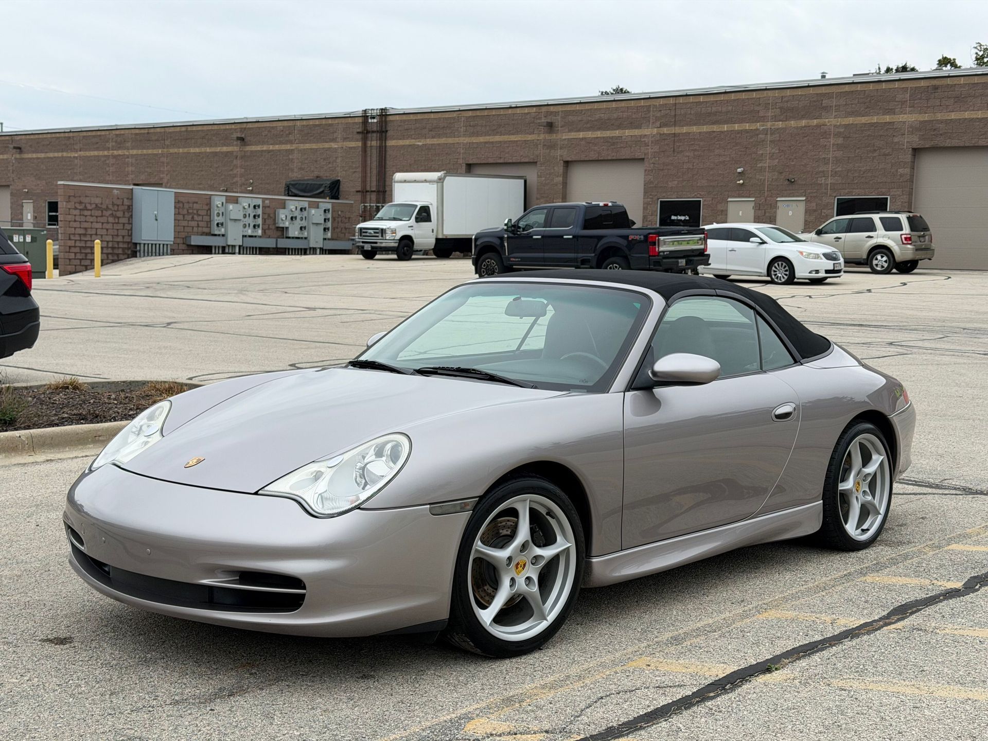 Silver Porsche convertible parked in front of a brick building on a sunny day.