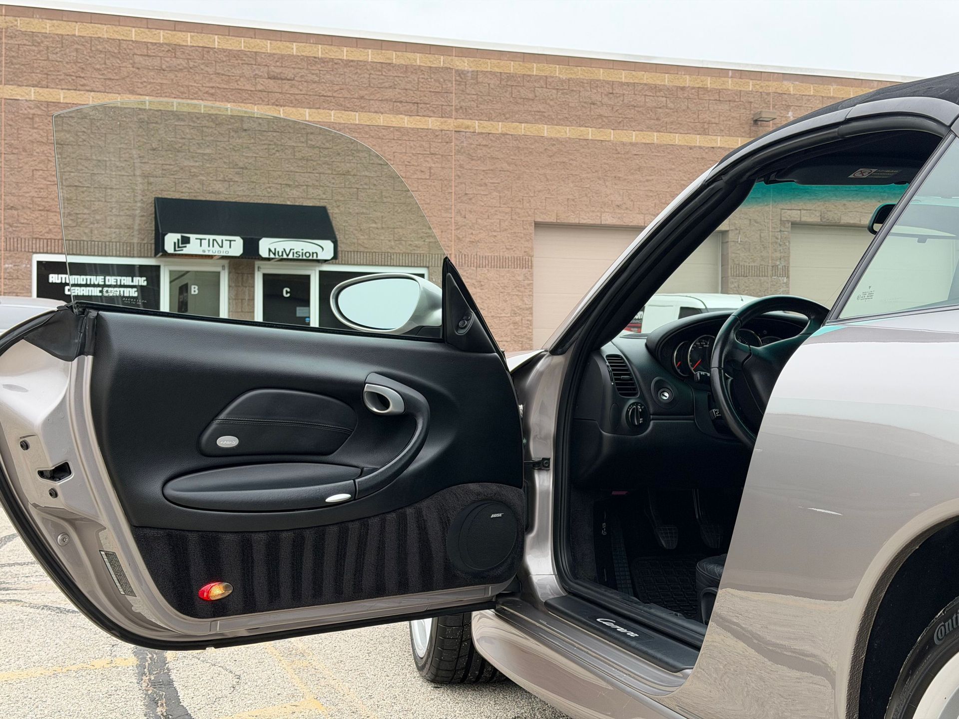 Open car door reveals interior details, side mirror, and building exterior.