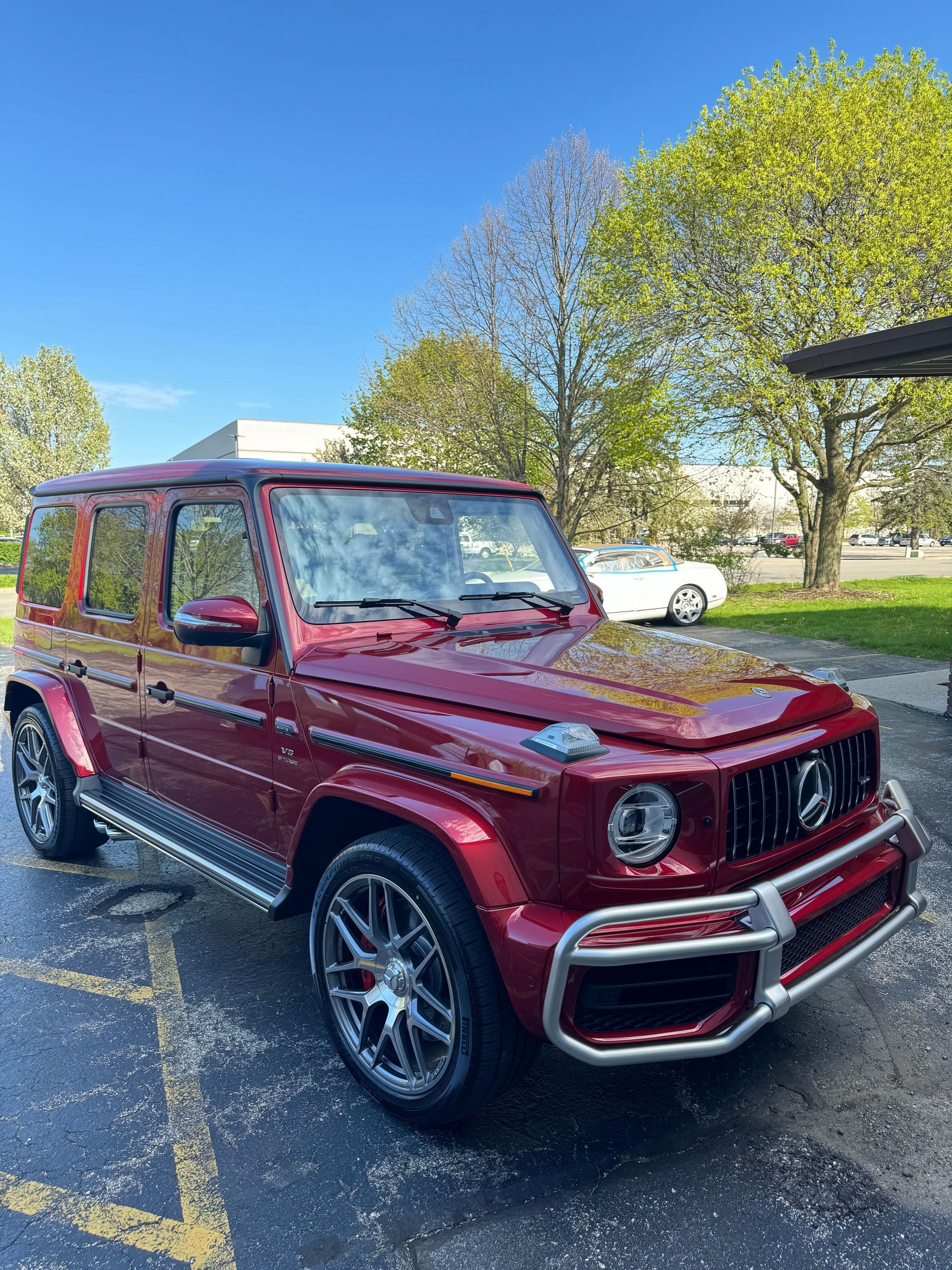 Red Mercedes G-Class SUV parked on asphalt. Shiny paint, chrome accents, and a blue sky background.